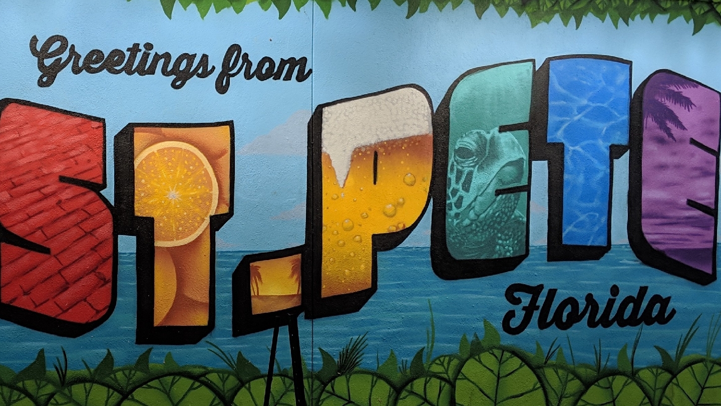 A bright painted mural reading Greetings from St. Pete, Florida, in the salon’s downtown neighborhood.